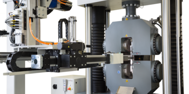 Sistema de ensayos automatizado roboTest P durante la alimentación de una probeta de metal en una máquina de ensayos de materiales