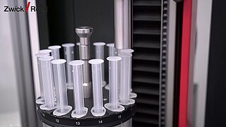 Materials testing machine with rotating magazine for syringe testing