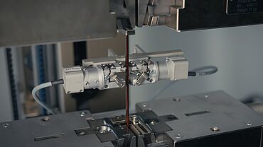 Detailaufnahmen eines isolierten Kupferdrahtes für E-Motoren im Zugversuch-Aufbau mit Hochpräzisions-Extensometer für die E-Modul BestimmungE-Motor Prüfung: Zugversuch an insoliertem Kupferdraht mit Hochpräzisions-Extensometer zur Bestimmung des elastischen Bereiches (E-Modul, Youngscher Modul)
