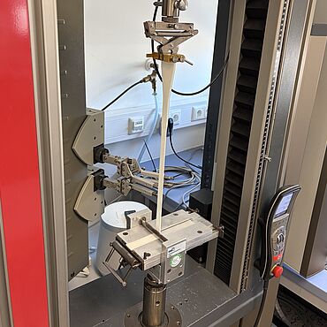 Seitenansicht des eingespannten Prüfaufbaus in einer Materialprüfmaschine für den 90°-Abzugsversuch