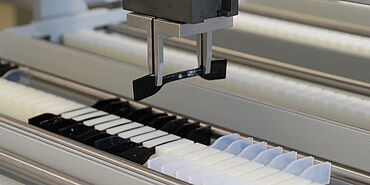 Het roboTest L geautomatiseerd testsysteem neemt een elastomeer sample uit het sample magazijn.