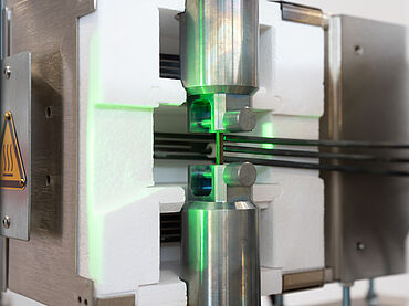 Detaiaufnahme des Prüfaufbaus für den Hochtemperatur-Zugversuch an Mikroprobe mit Hochtemperaturofen, starrem Gestänge, videoXtens 1-32 HP/TZ und Kappa Kriechprüfmaschine von ZwickRoell