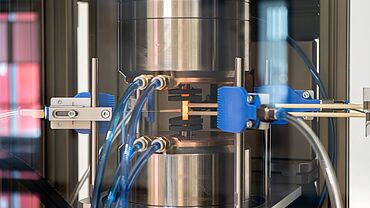 Detailed view of the test arrangement for thermomechanical fatigue tests. The testing system is equipped with an induction heating system, cooling nozzles, ribbon thermocouples for measurement of the specimen temperature and a contact-type strain measurement system.